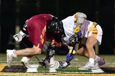 Two men are playing lacrosse on a field.