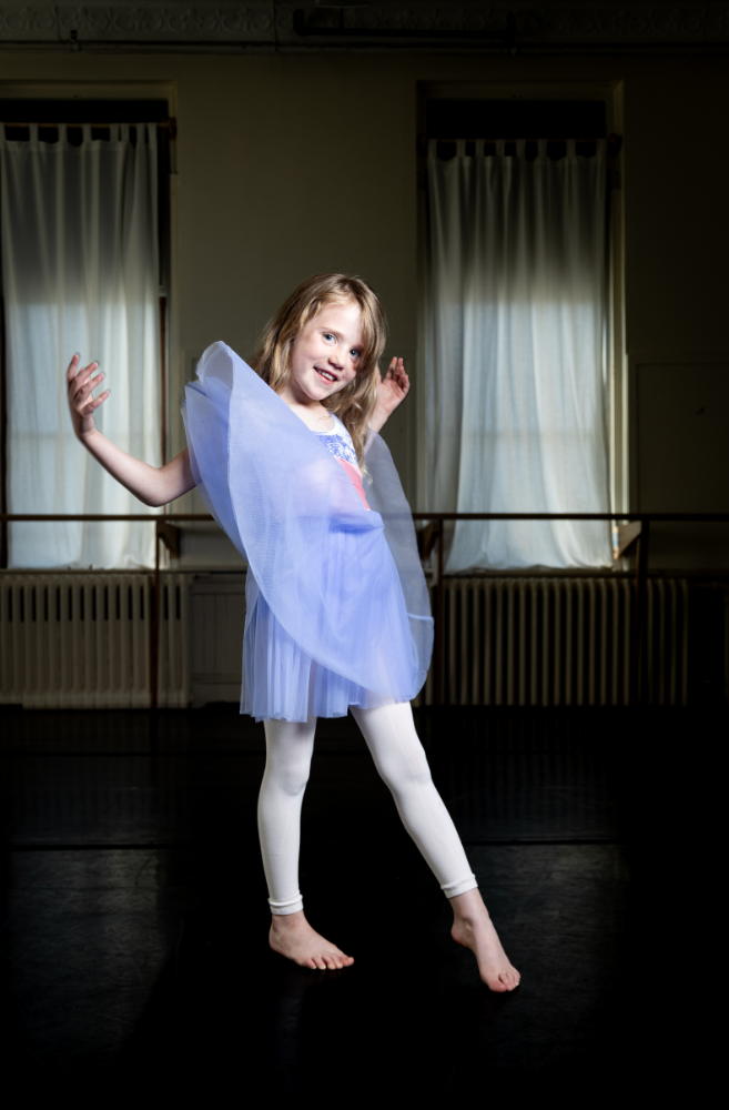 A little girl in blue dress and white tights.